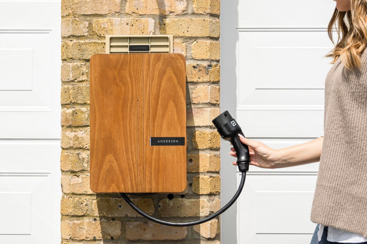 Wall-mounted home EV charger beside a garage door with the plug in hand